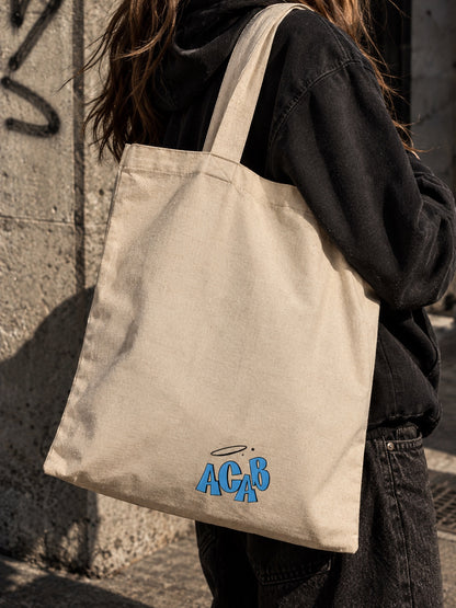 Πίσω πλευρά μπεζ tote bag με μπλε γράμματα ACAB και φωτοστέφανο