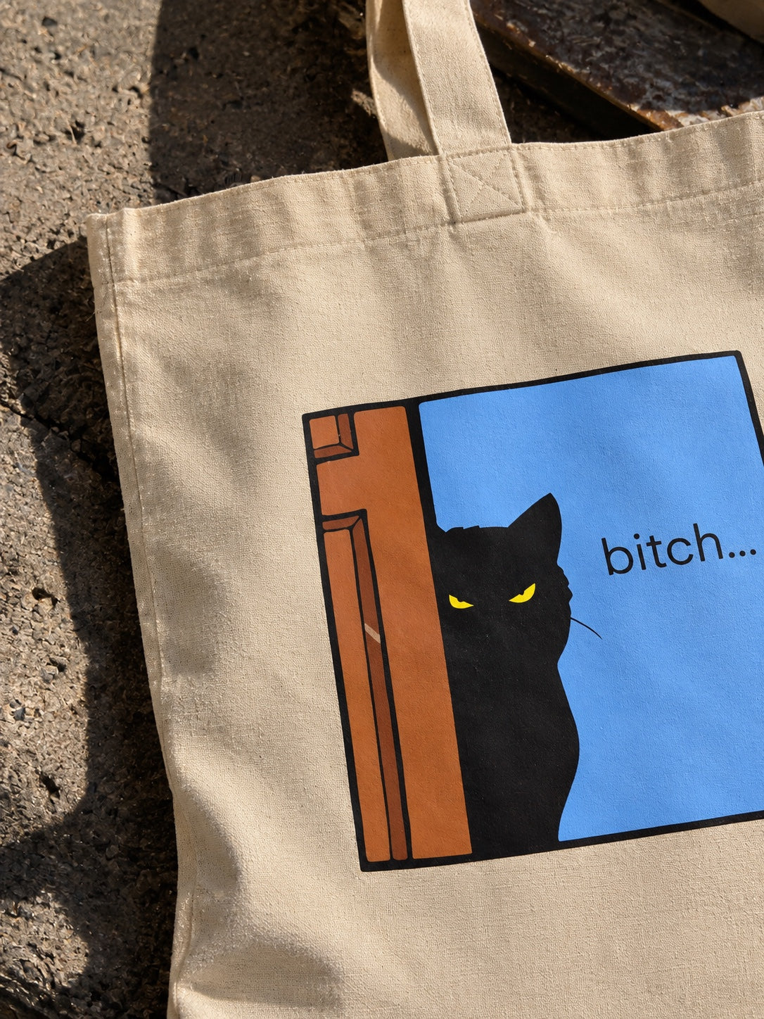 Μπεζ tote bag με μαύρη γάτα με κίτρινα μάτια πίσω από πόρτα και τη φράση bitch