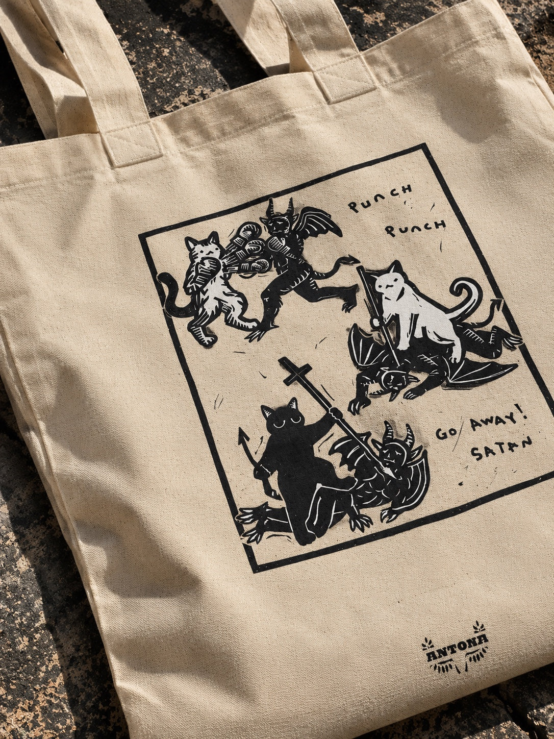 Κοντινή φωτογραφία tote bag με ασπρόμαυρο σχέδιο γάτων που πολεμούν δαίμονες