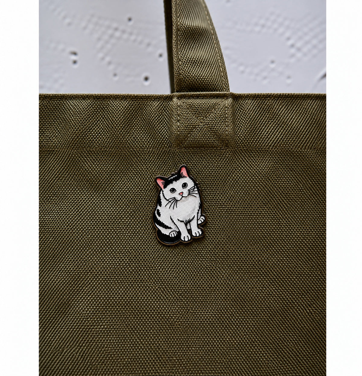 Cute black and white cat wooden printed pin displayed on an olive green bag