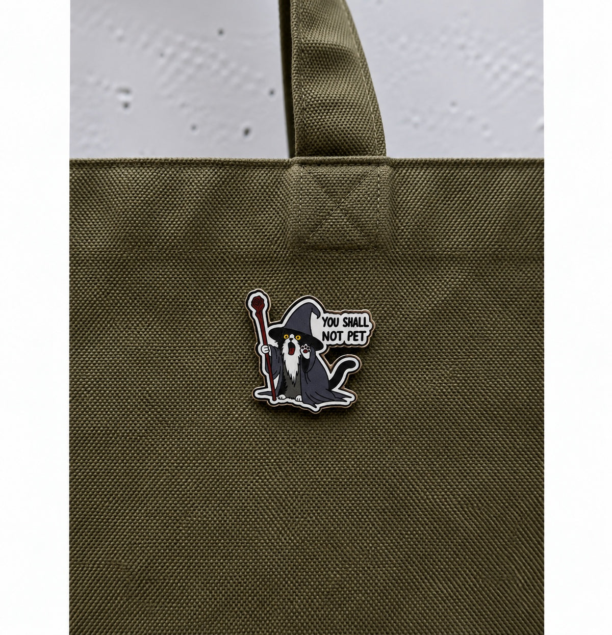 Wizard cat pin with the phrase You Shall Not Pet displayed on an olive green bag